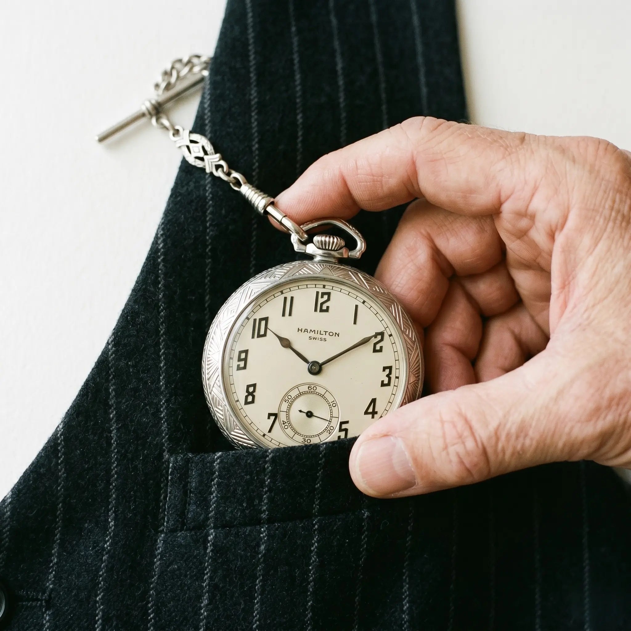 Art Deco style 1920s silver pocket watch drawn from a pinstriped vest. Image