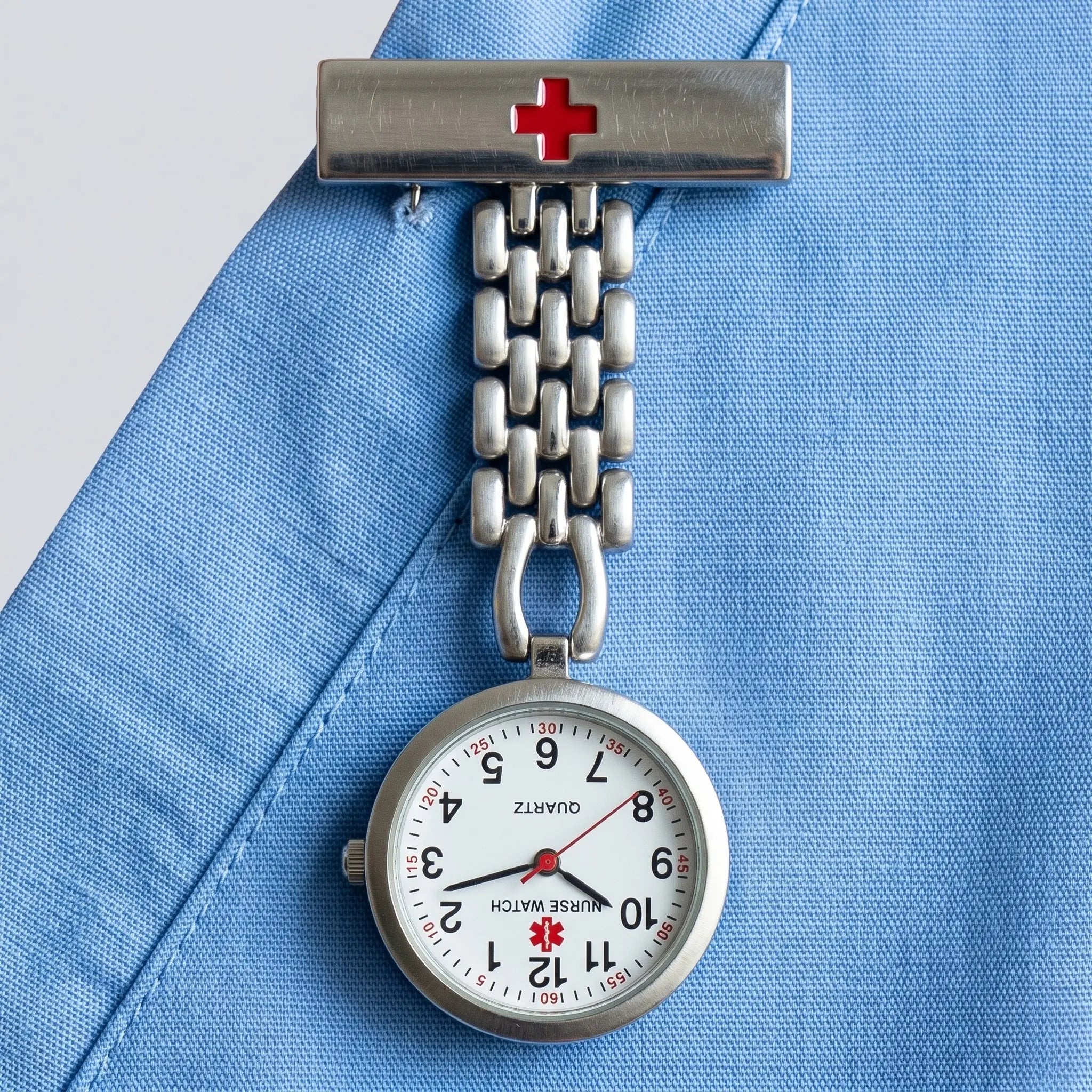 Stainless steel fob-style nurse watch pinned to a light blue medical scrub top. Image