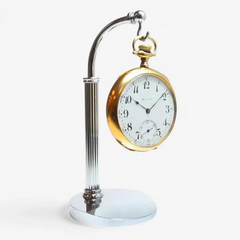 A vintage gold-toned pocket watch with white dial and black numerals displayed on an elegant chrome stand