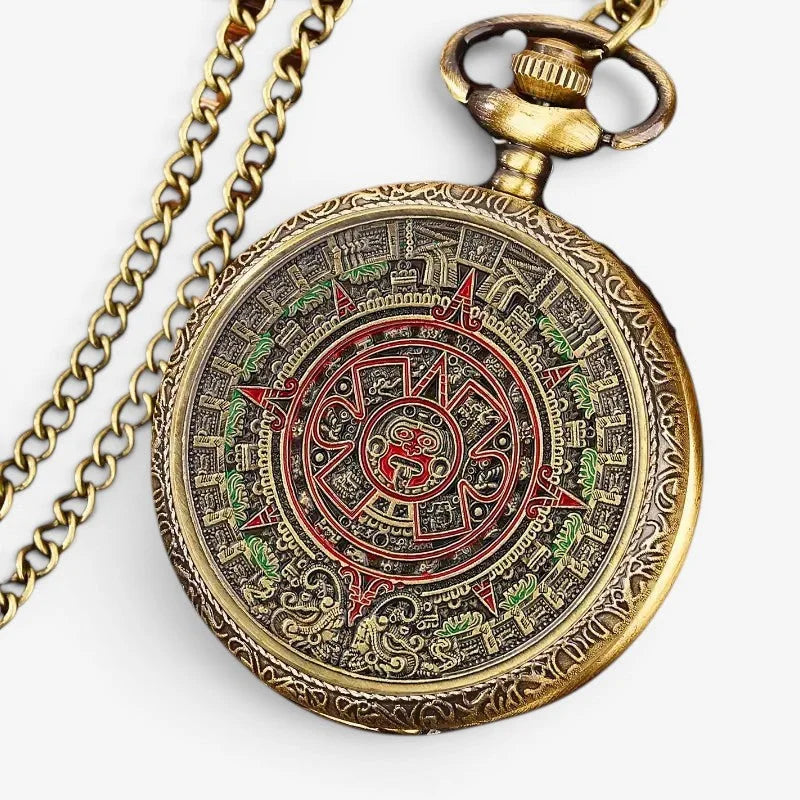 Antique brass aztec pocket watch with intricate calendar design and red and green enameled details on circular face