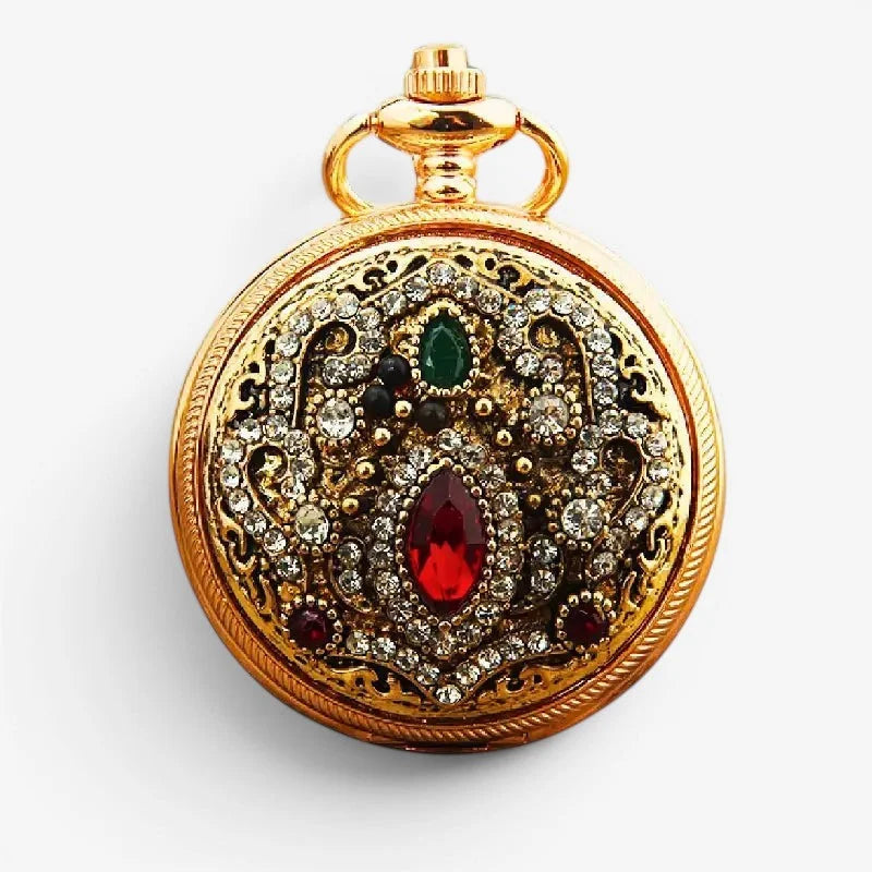 Gold-colored diamond pocket watch with intricate filigree design adorned with clear crystals and red and green gemstones