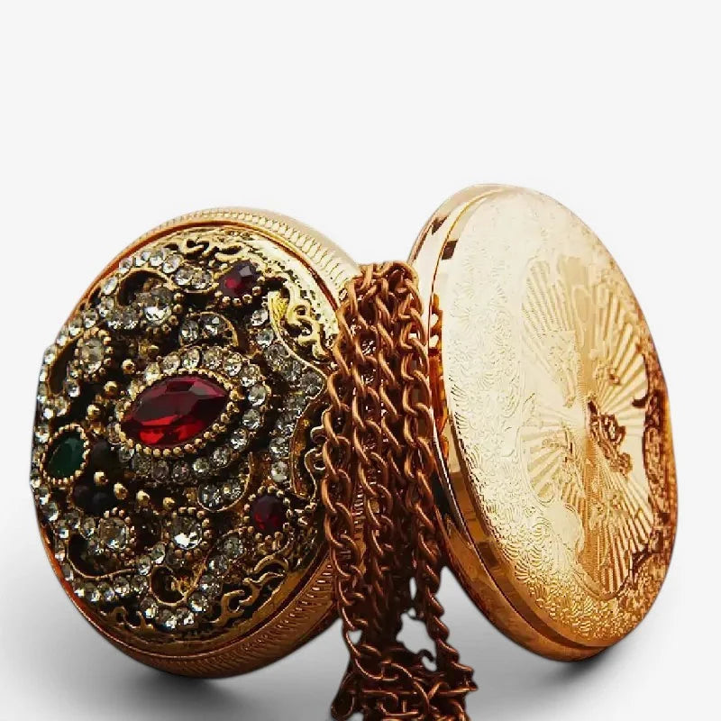 Diamond pocket watch with a gold-toned ornate locket featuring a central red gemstone and clear green stones filigree design