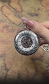 A men's silver mechanical pocket watch displaying its internal gear movement