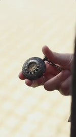 A man in a classic grey tweed blazer pulls a black men's steampunk steel pocket watch from his pocket by its chain, opening the front cover to reveal the exposed mechanical gold gears inside
