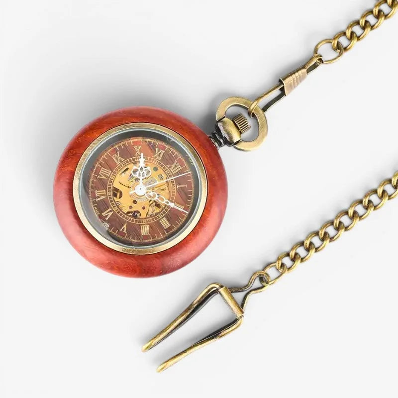 Red wooden pocket watch with brass chain and roman numerals on visible face featuring a decorative fork