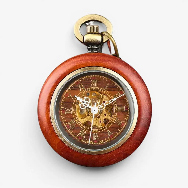 A vintage red wooden pocket watch with gold accents and roman numeral markings on a transparent face