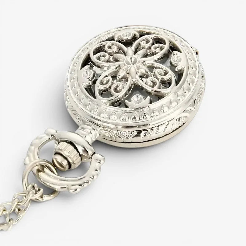 Small antique silver-toned pocket watch showing ornate floral filigree design on its back with a decorative chain attached